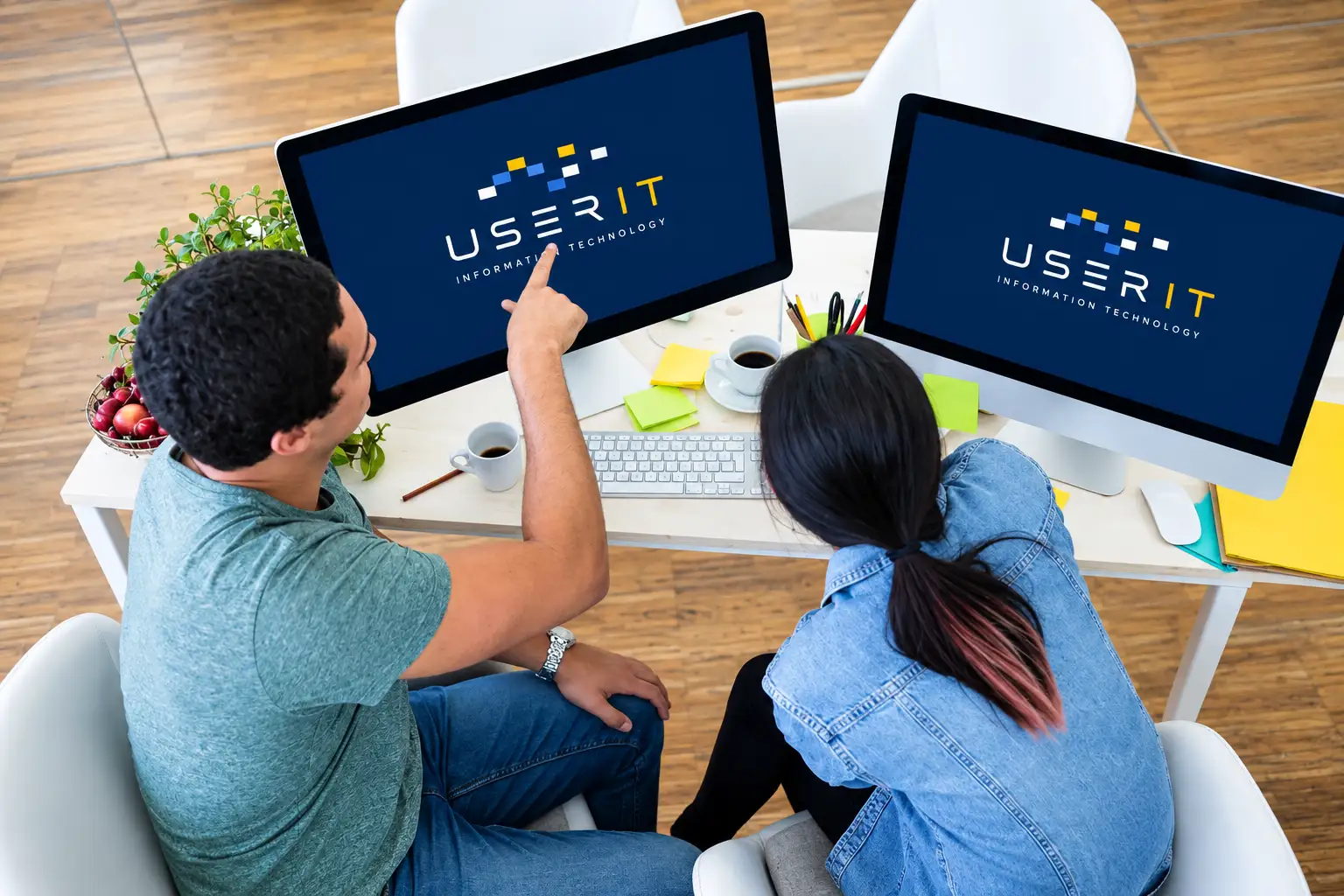 Dos personas, vistas desde arriba, comentan dos monitores que muestran el logotipo de UserIT